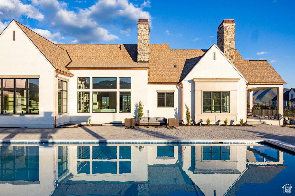 Rear view of property featuring a patio area, an outdoor pool, a chimney, and roof with shingles