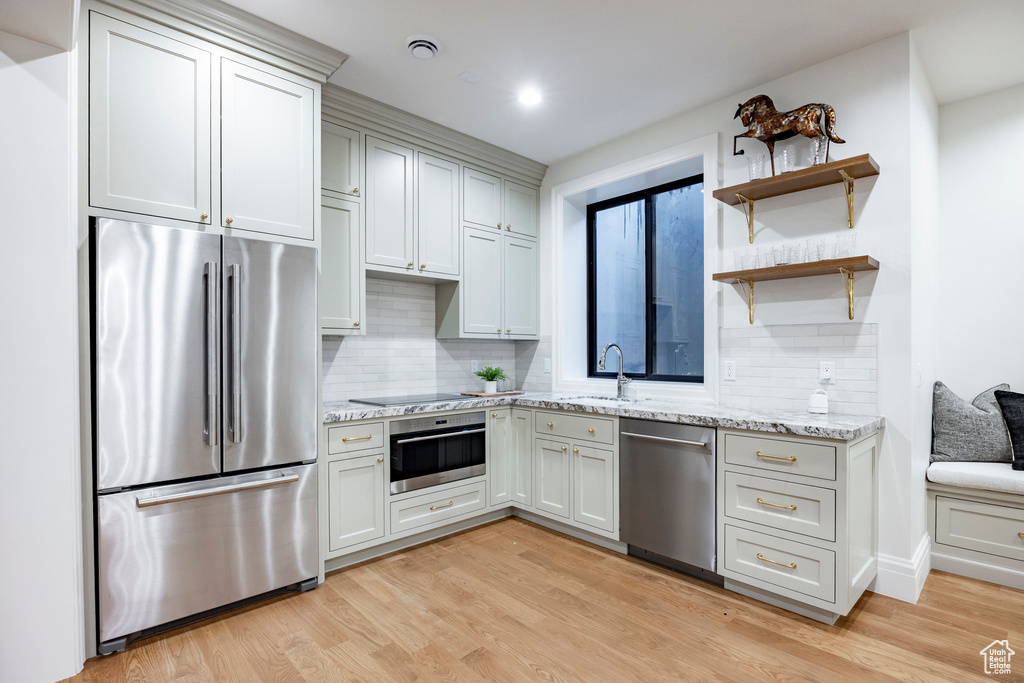 Kitchen with appliances with stainless steel finishes, a sink, backsplash, light wood-style flooring, and light stone countertops