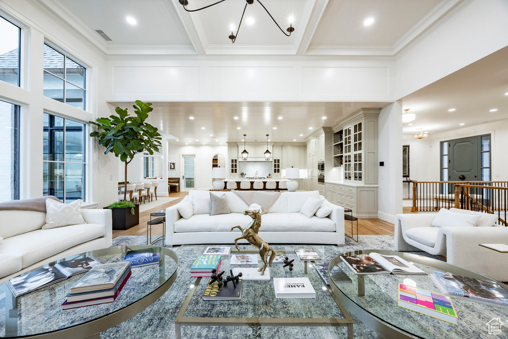 Living area with a chandelier, a towering ceiling, light wood-style floors, ornamental molding, and recessed lighting