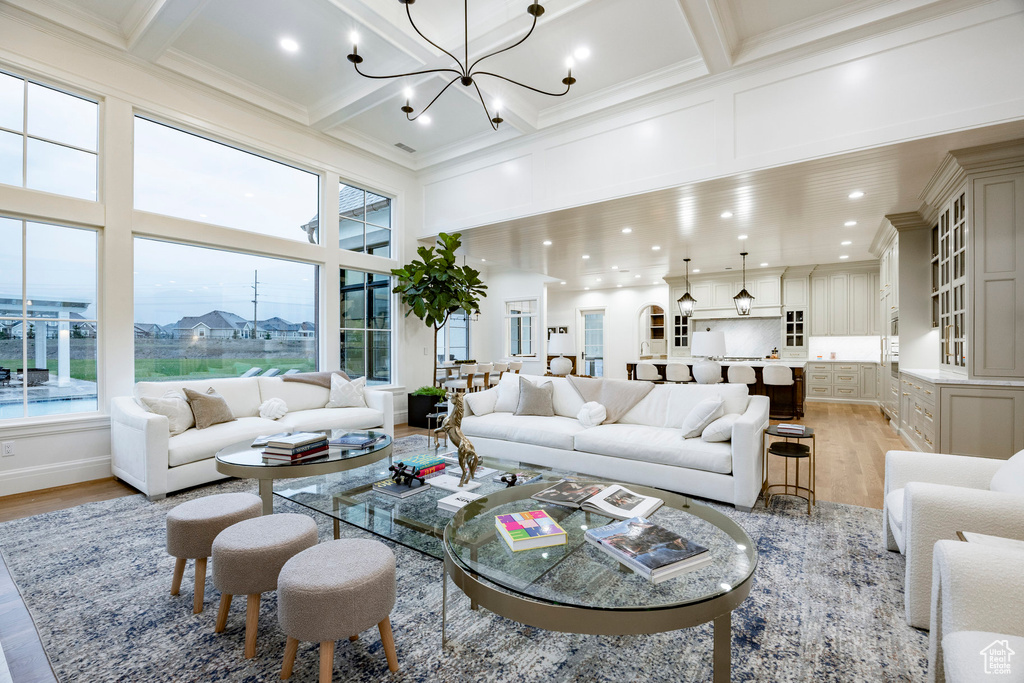 Living room with light wood-style floors, a towering ceiling, healthy amount of natural light, a chandelier, and beamed ceiling