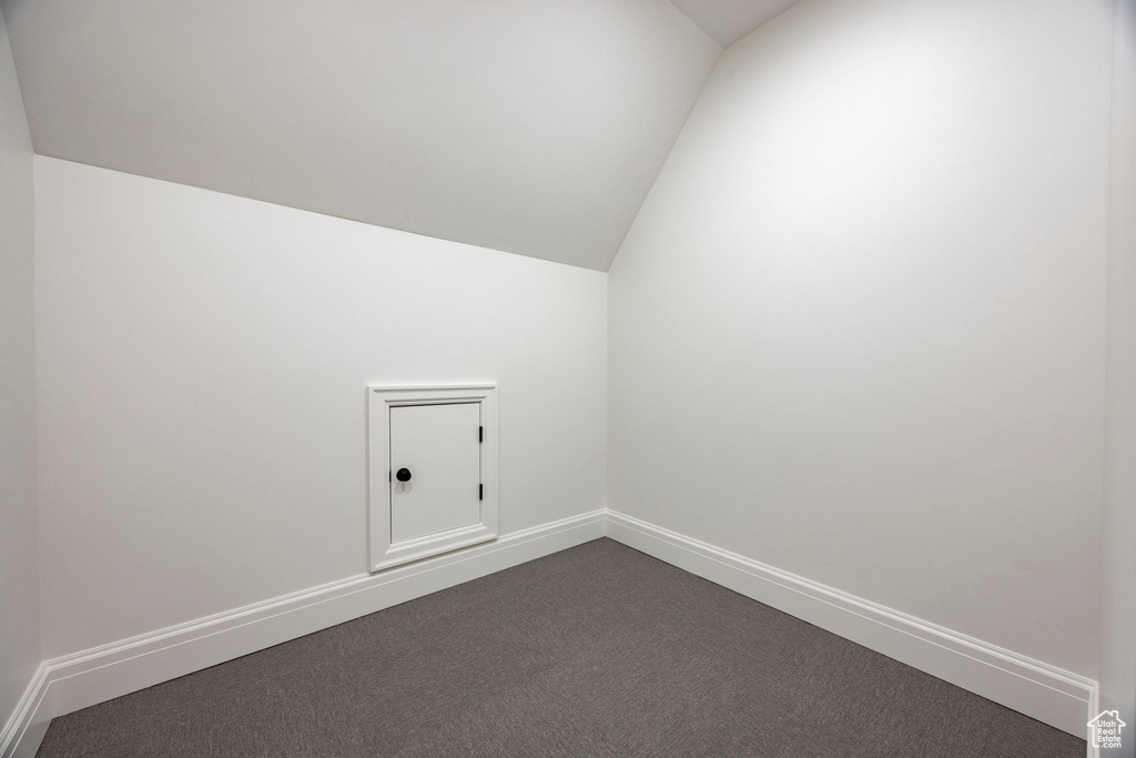 Additional living space with lofted ceiling, dark colored carpet, and baseboards