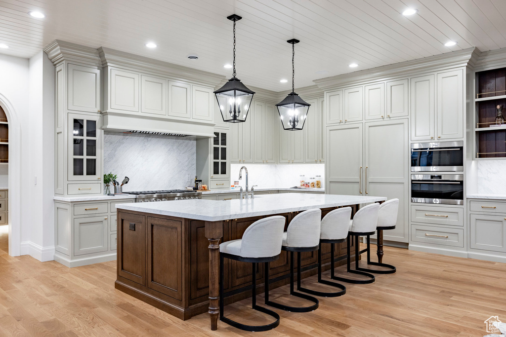 Kitchen featuring a kitchen breakfast bar, light wood finished floors, a center island with sink, recessed lighting, and backsplash