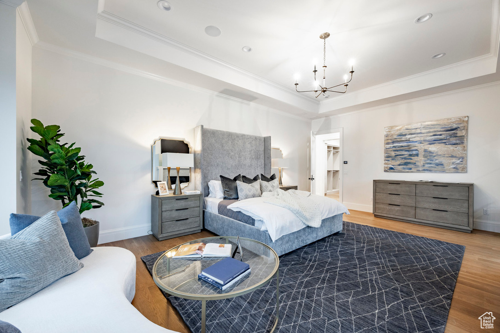 Bedroom featuring a tray ceiling, a chandelier, ornamental molding, wood finished floors, and baseboards