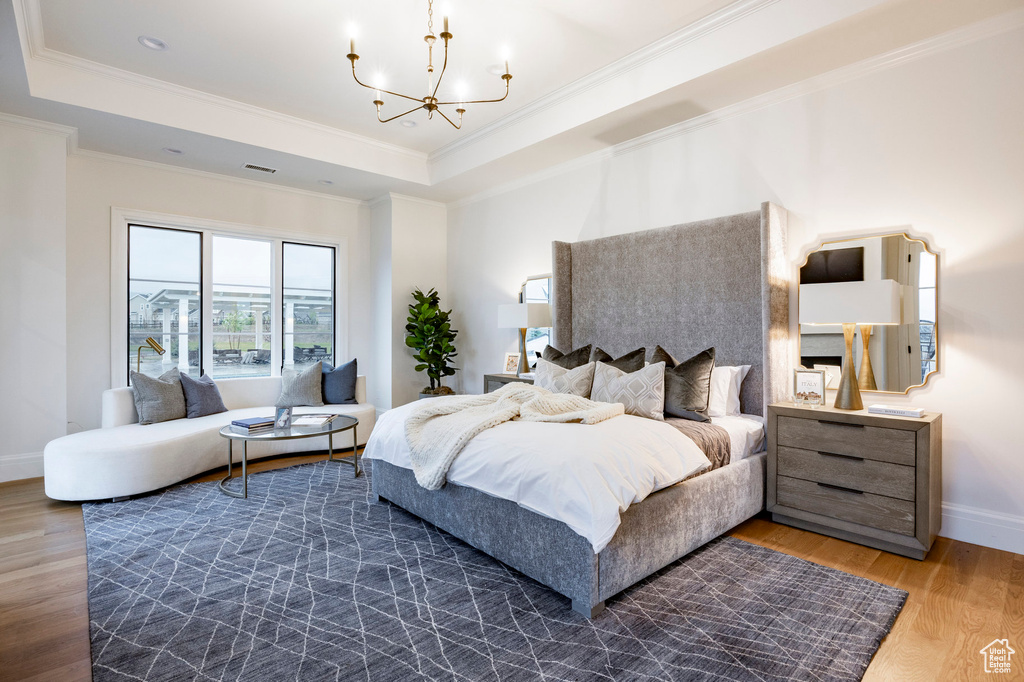 Bedroom with a raised ceiling, a chandelier, wood finished floors, crown molding, and baseboards
