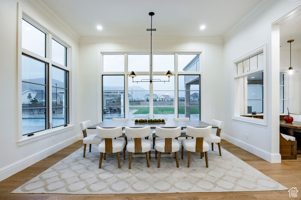 Dining room with plenty of natural light, baseboards, ornamental molding, wood finished floors, and a chandelier
