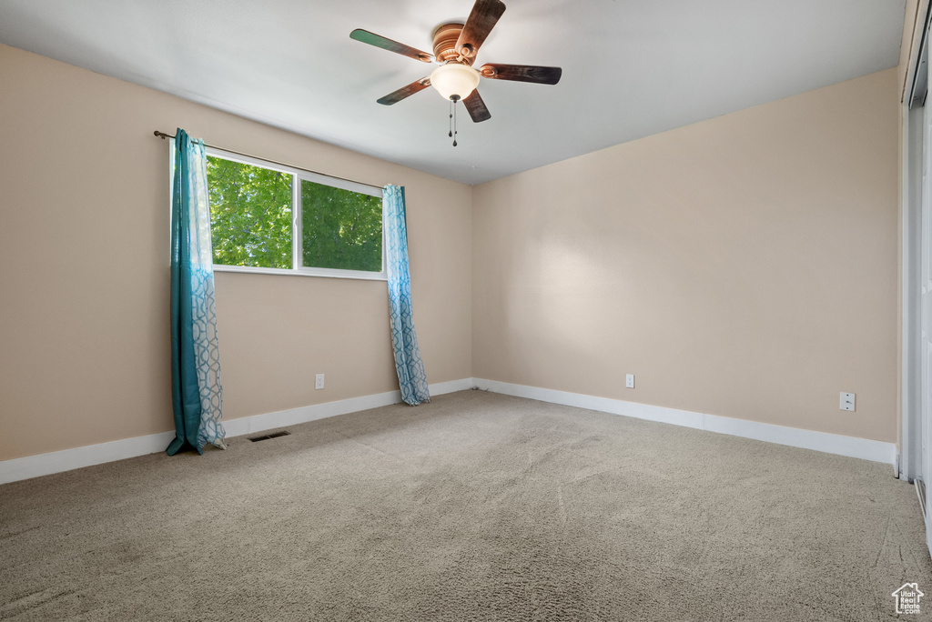 Carpeted empty room featuring ceiling fan and baseboards
