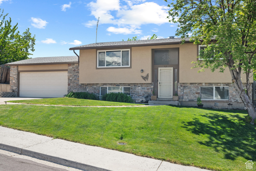 Bi-level home featuring stucco siding, stone siding, an attached garage, and a front yard