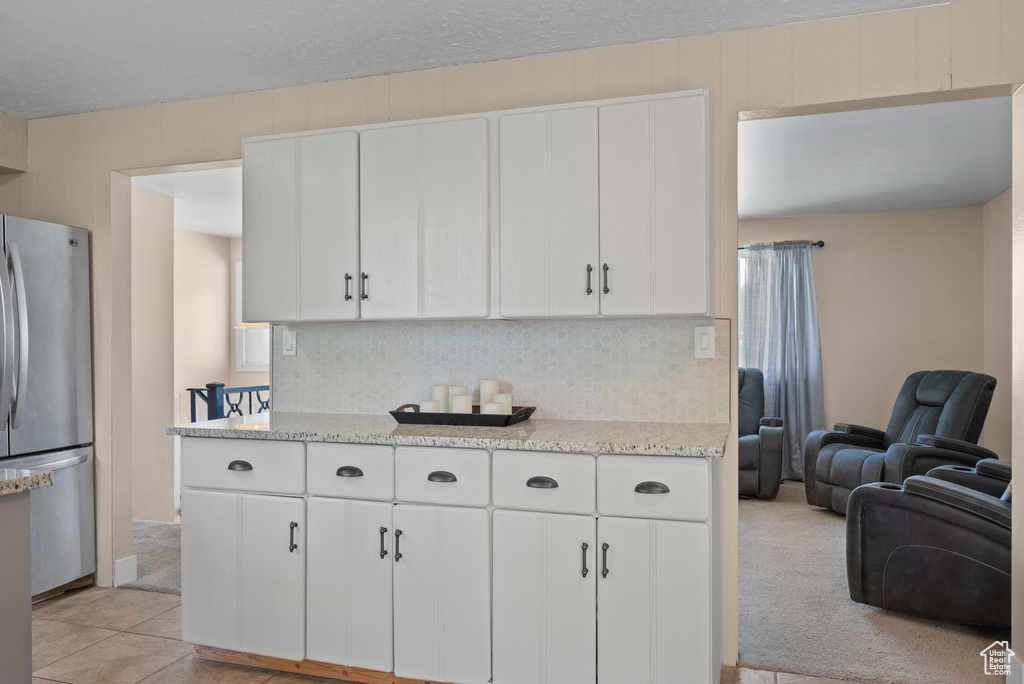 Kitchen featuring freestanding refrigerator, decorative backsplash, white cabinetry, and open floor plan