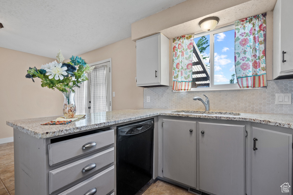 Kitchen with black dishwasher, a sink, a peninsula, decorative backsplash, and gray cabinets