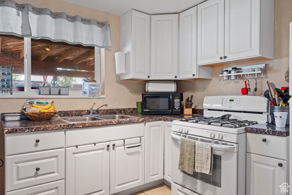 Kitchen with gas range gas stove, black microwave, a sink, and white cabinetry
