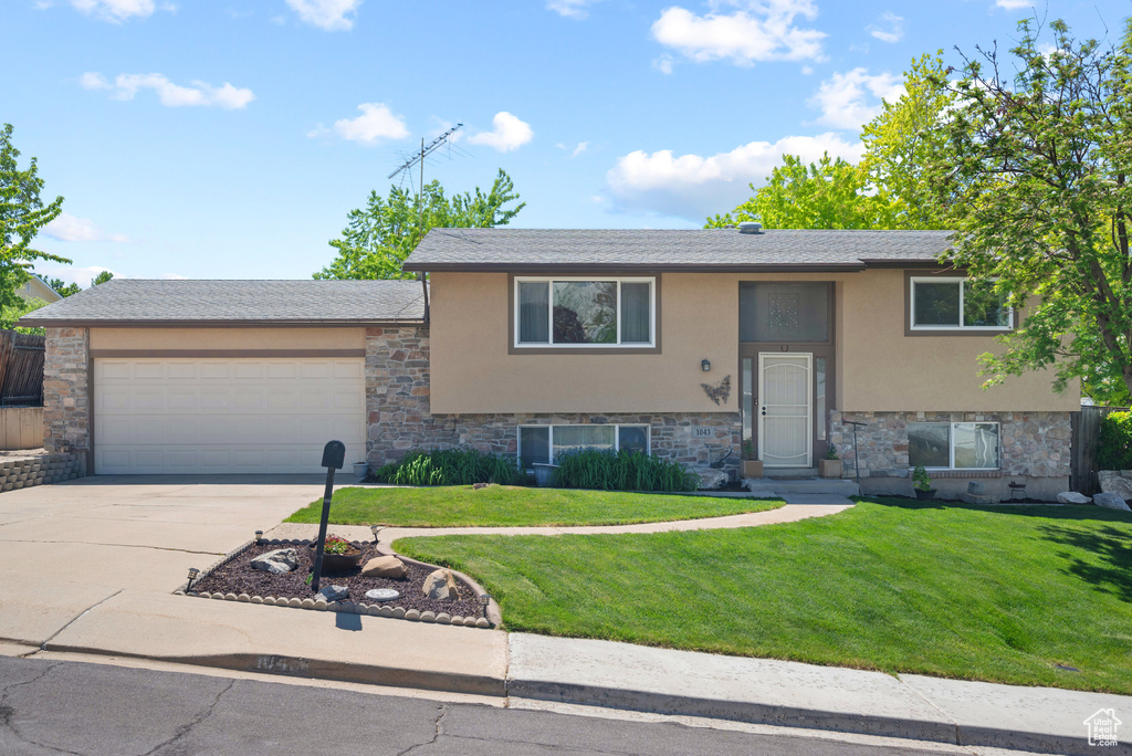 Bi-level home featuring stucco siding, stone siding, an attached garage, and concrete driveway