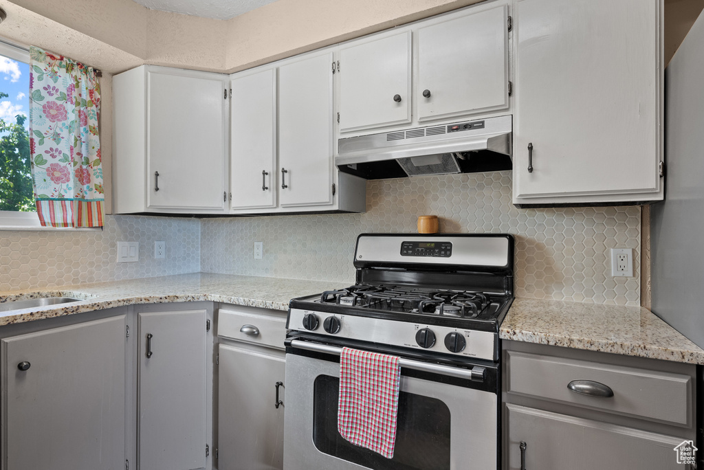 Kitchen featuring stainless steel range with gas stovetop, under cabinet range hood, backsplash, white cabinetry, and gray cabinets