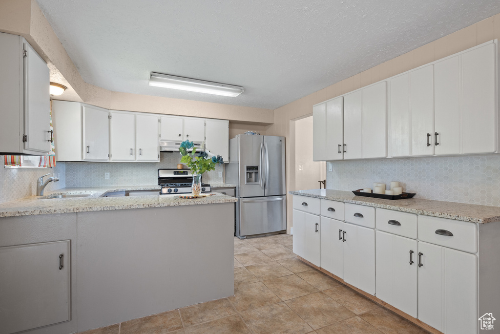Kitchen featuring appliances with stainless steel finishes, a sink, under cabinet range hood, decorative backsplash, and white cabinetry