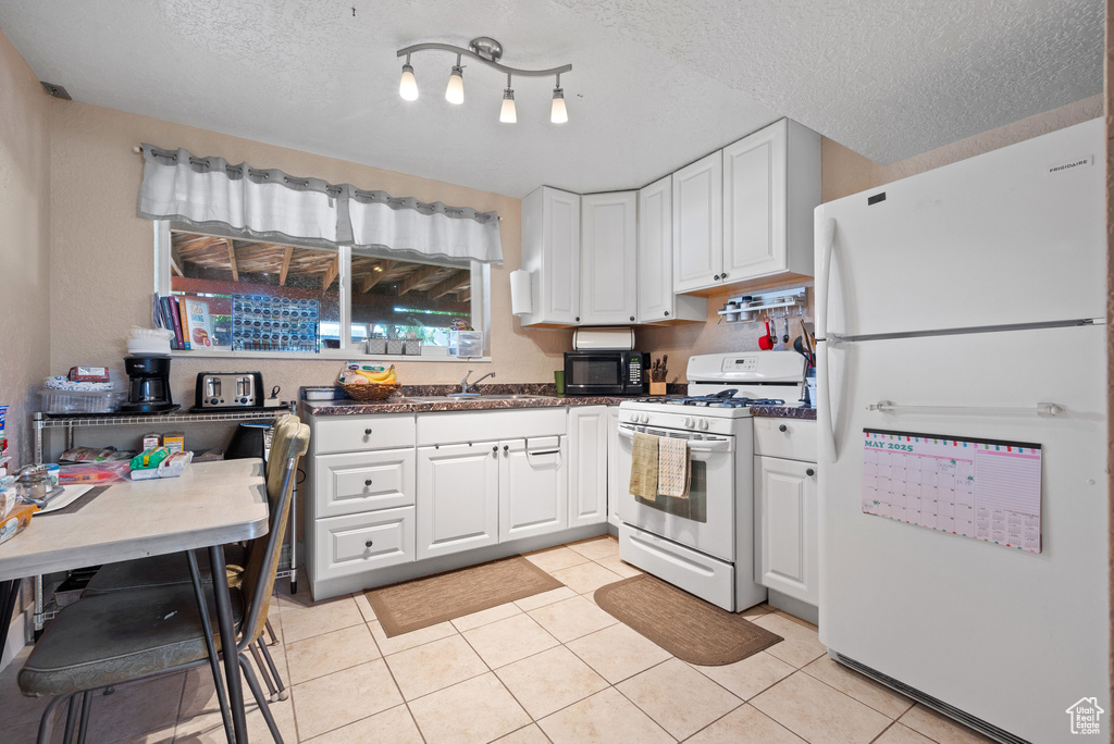 Kitchen featuring white appliances, white cabinets, light tile patterned floors, and a textured ceiling