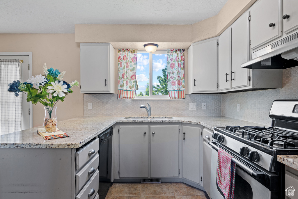 Kitchen featuring stainless steel gas range, a sink, under cabinet range hood, and backsplash