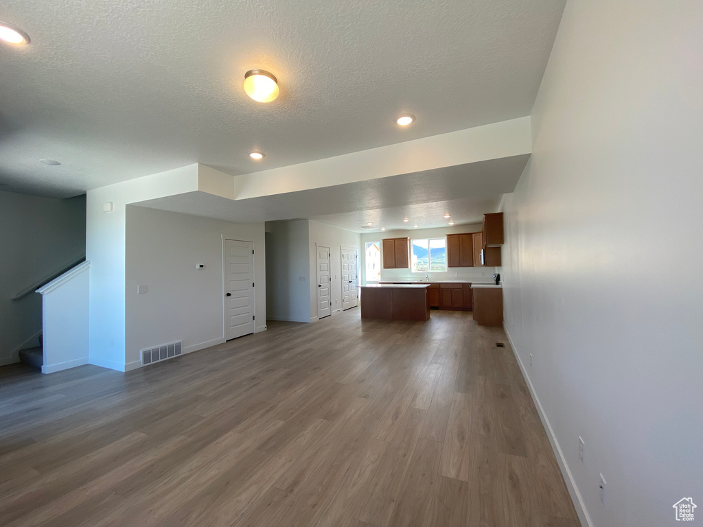 Unfurnished living room featuring baseboards, stairs, wood finished floors, a textured ceiling, and recessed lighting