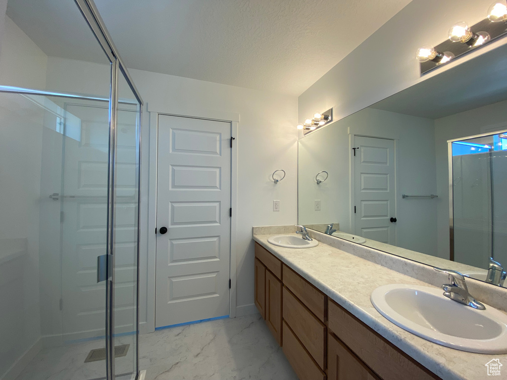 Bathroom with marble finish floors, a shower stall, double vanity, baseboards, and a textured ceiling