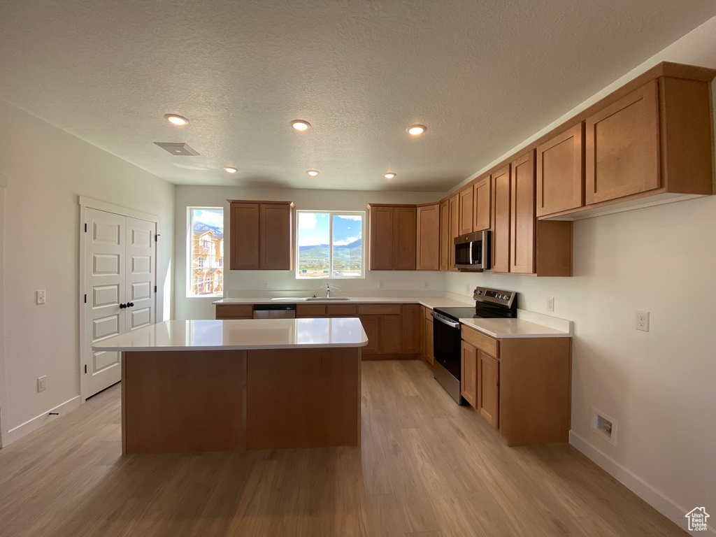 Kitchen with stainless steel appliances, a sink, light wood finished floors, a kitchen island, and light countertops