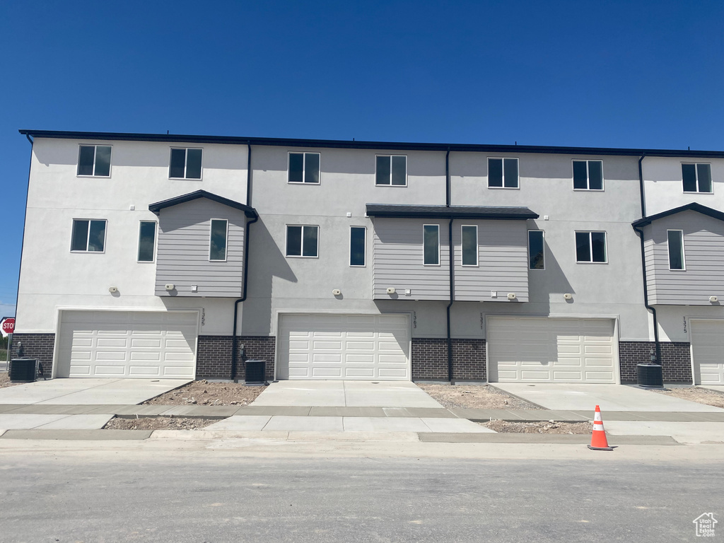 Townhome / multi-family property with stucco siding, a garage, cooling unit, and brick siding