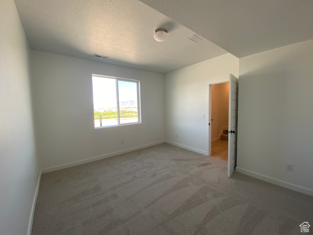 Empty room with light carpet, baseboards, and a textured ceiling