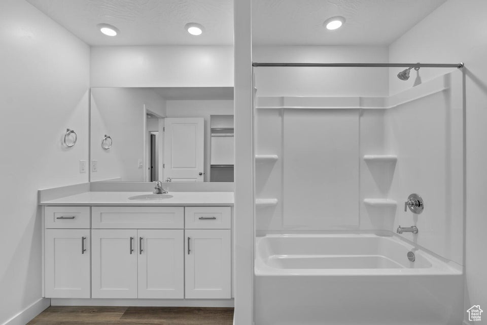 Full bath featuring wood finished floors, washtub / shower combination, vanity, and baseboards