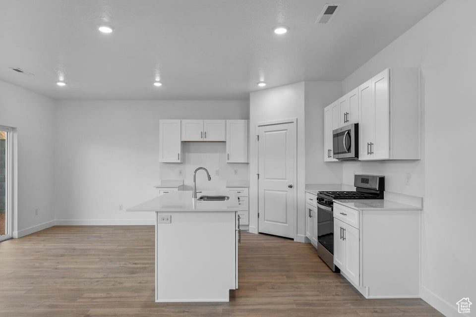 Kitchen with stainless steel appliances, a sink, an island with sink, baseboards, and wood finished floors