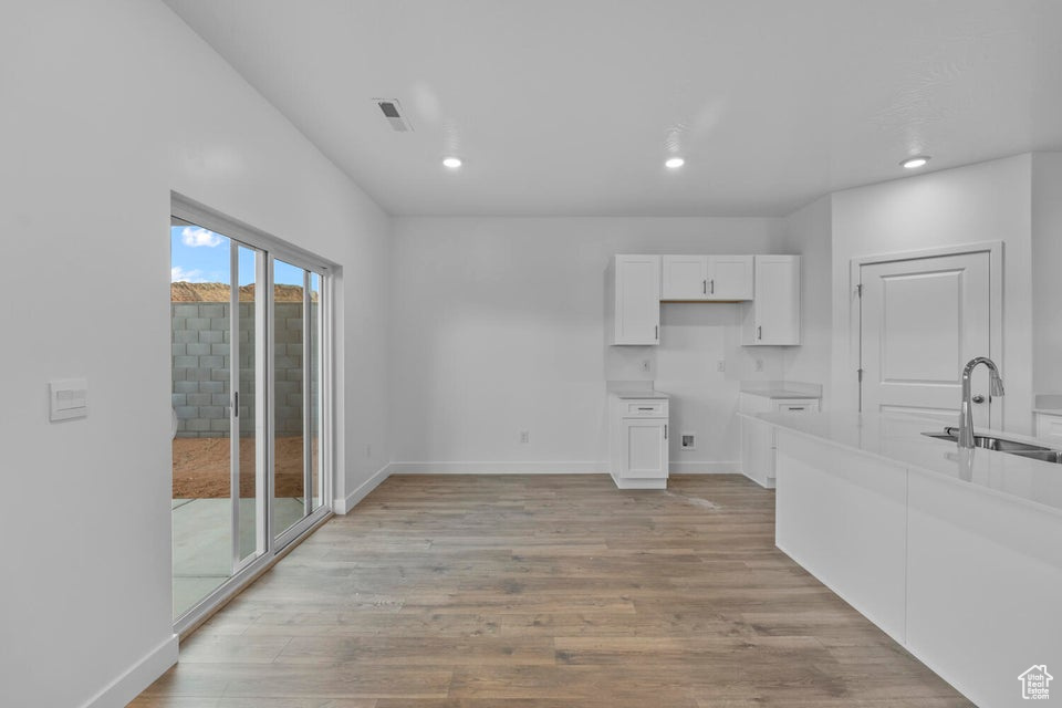 Kitchen featuring a sink, white cabinets, light wood-type flooring, baseboards, and recessed lighting