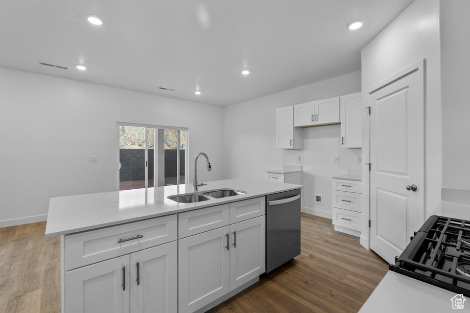Kitchen with a sink, stainless steel dishwasher, white cabinetry, wood finished floors, and recessed lighting