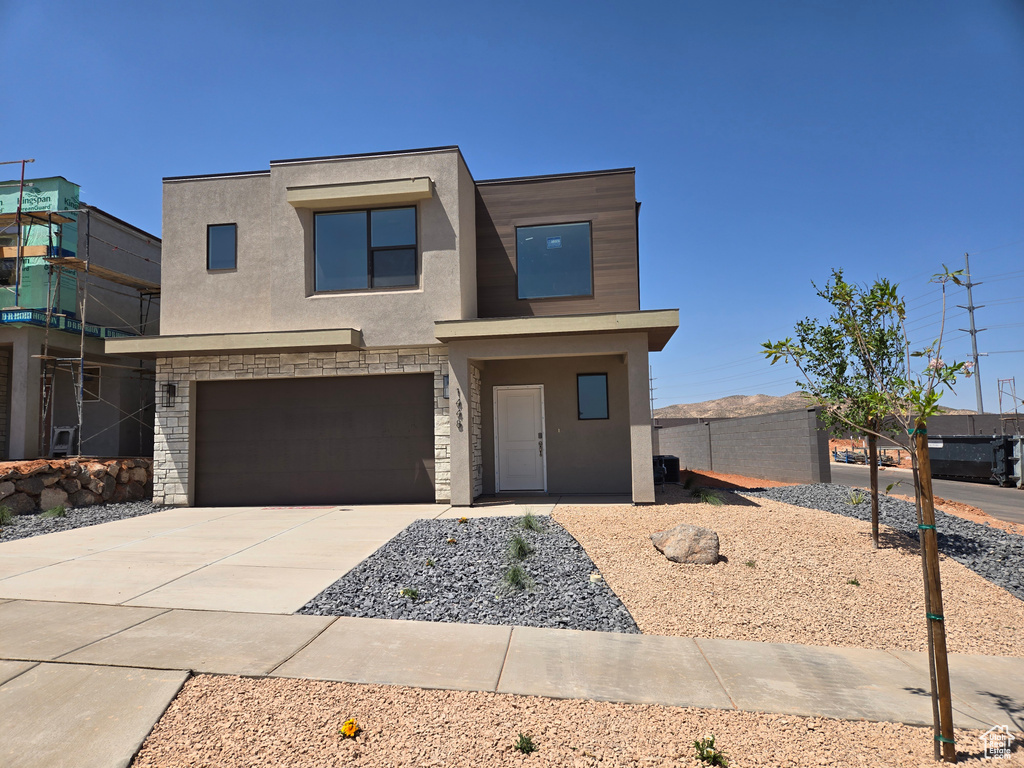 View of front facade with stucco siding, driveway, an attached garage, and stone siding