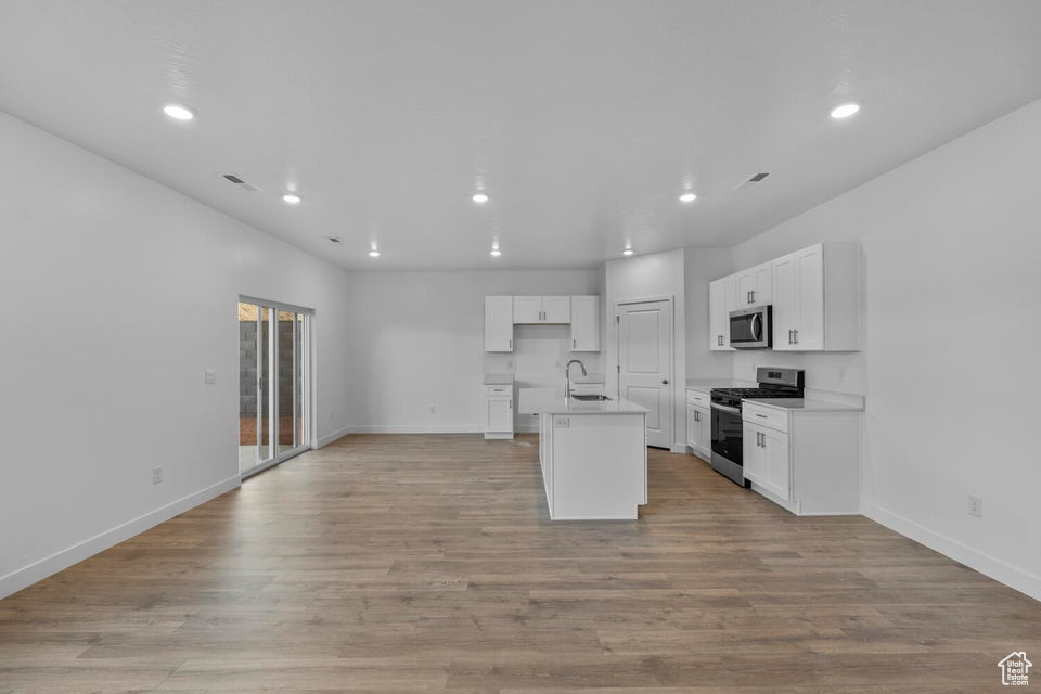 Kitchen featuring appliances with stainless steel finishes, a sink, open floor plan, recessed lighting, and white cabinets