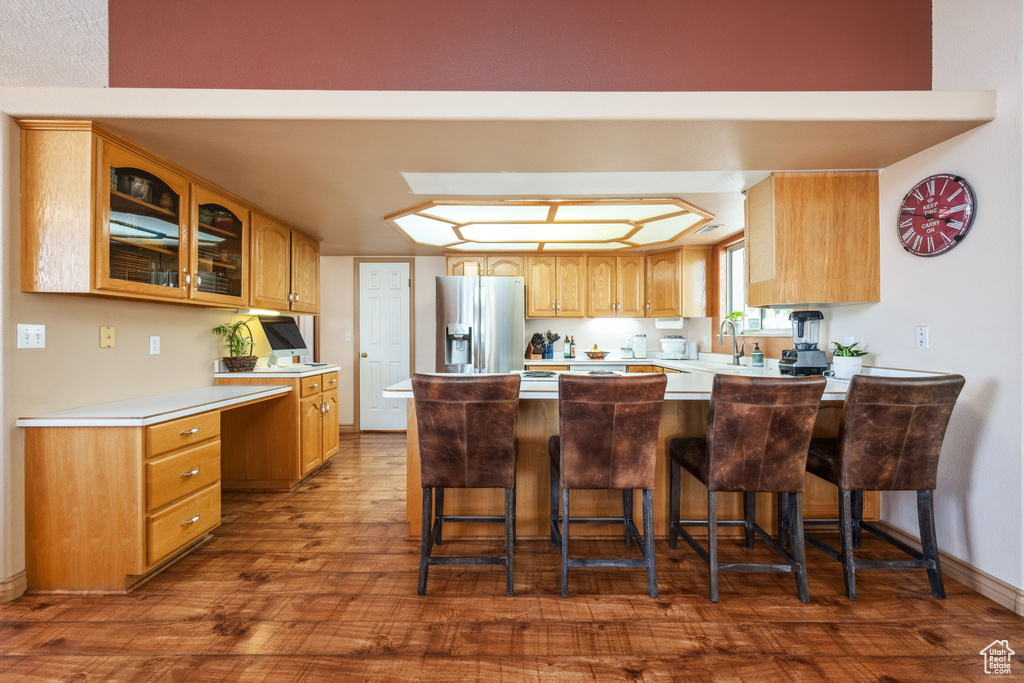 Kitchen featuring stainless steel refrigerator with ice dispenser, glass insert cabinets, dark wood-style floors, a peninsula, and a sink