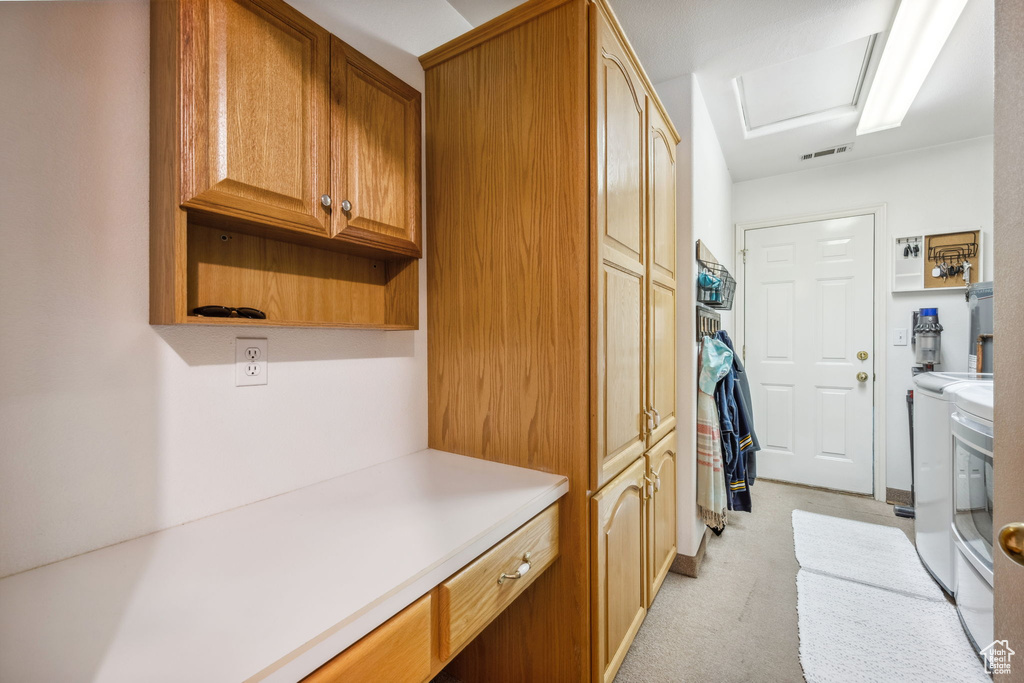Clothes washing area with cabinet space, washing machine and dryer, and light colored carpet