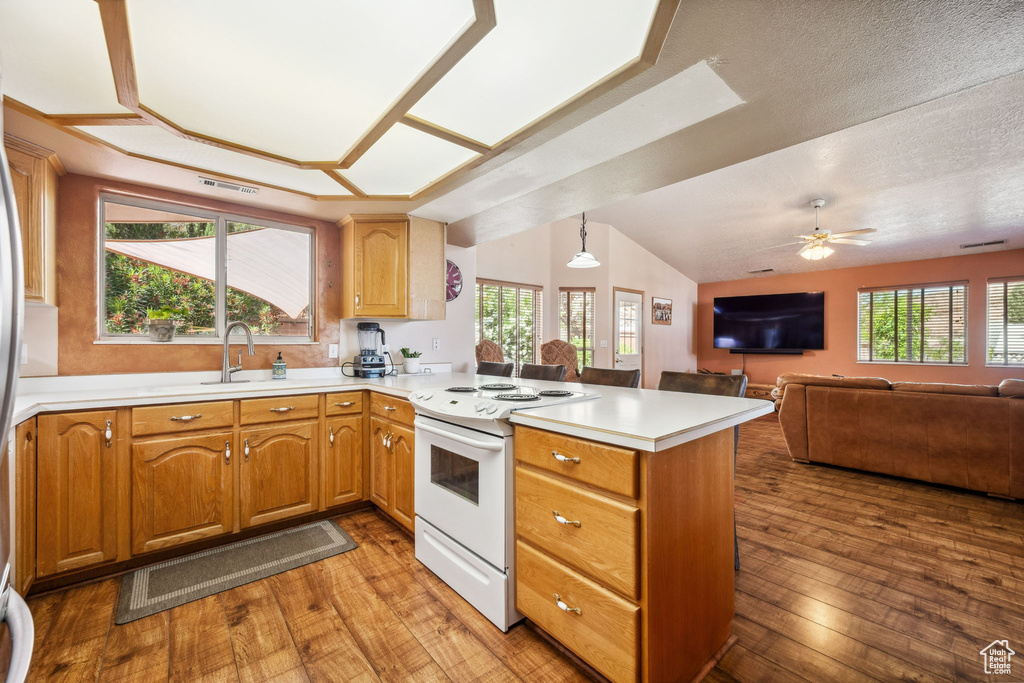 Kitchen with white electric stove, a peninsula, a sink, light countertops, and hardwood / wood-style flooring