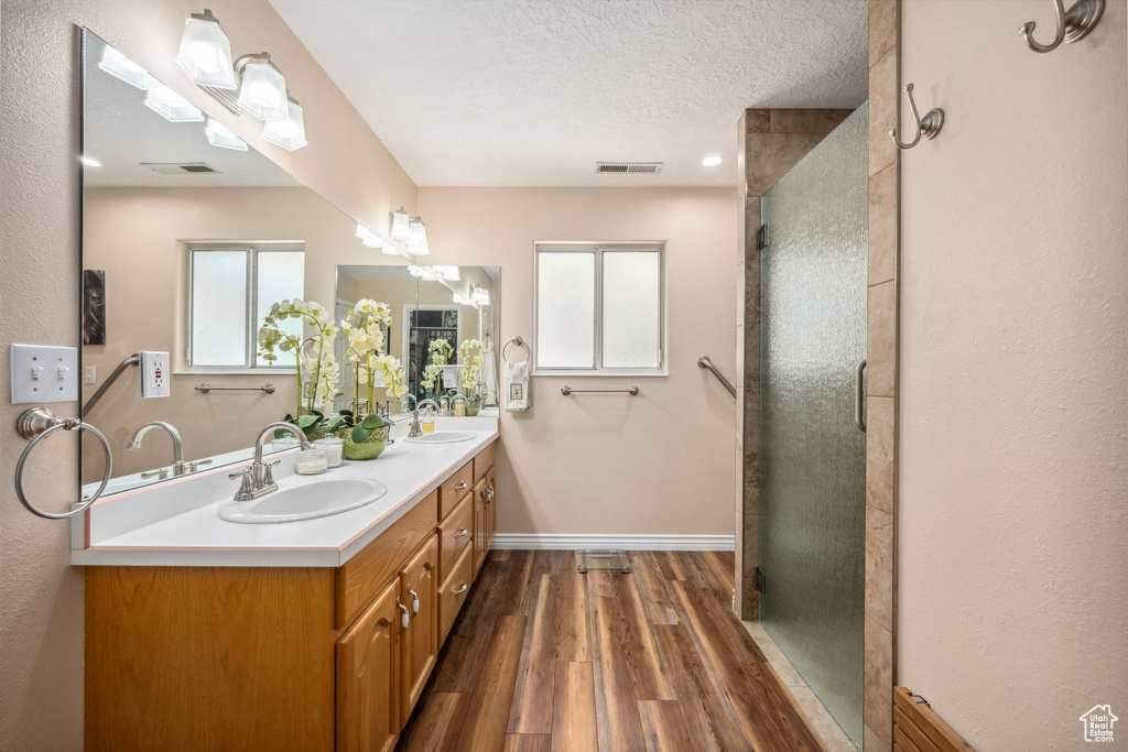 Bathroom with wood finished floors, a shower stall, baseboards, double vanity, and a textured ceiling
