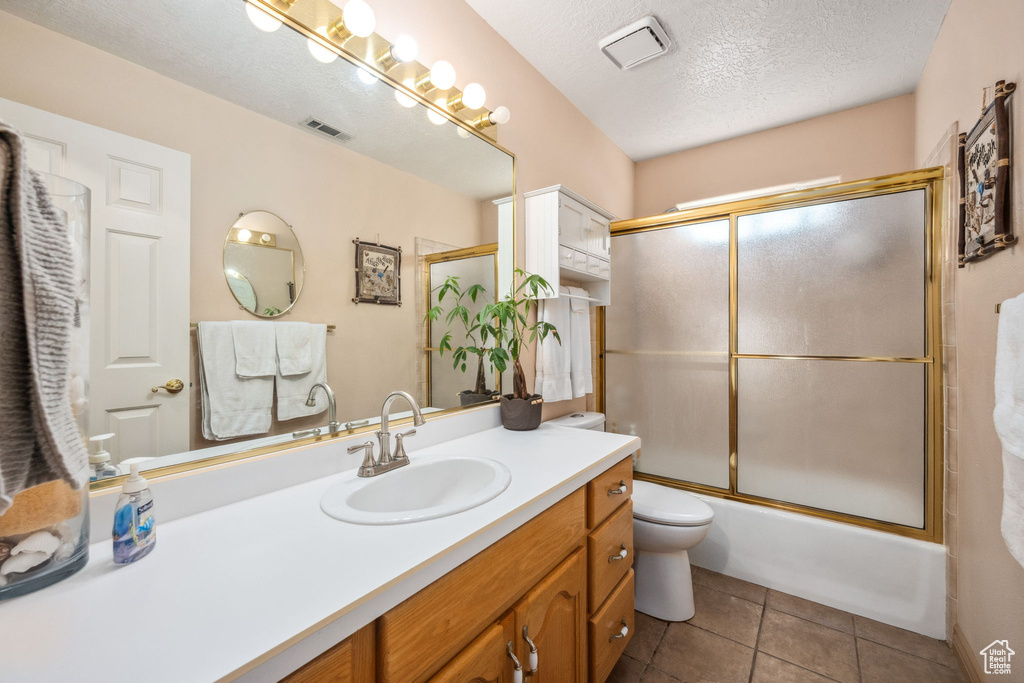 Bathroom featuring vanity, a textured ceiling, combined bath / shower with glass door, toilet, and tile patterned flooring