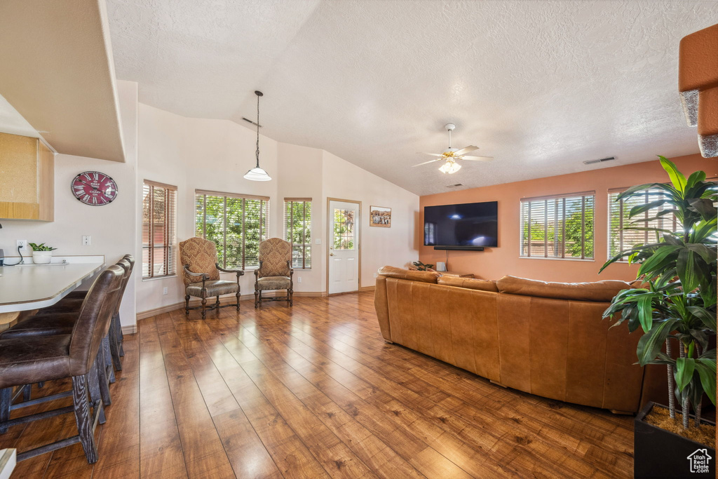 Living room featuring wood-type flooring, lofted ceiling, a ceiling fan, a textured ceiling, and baseboards