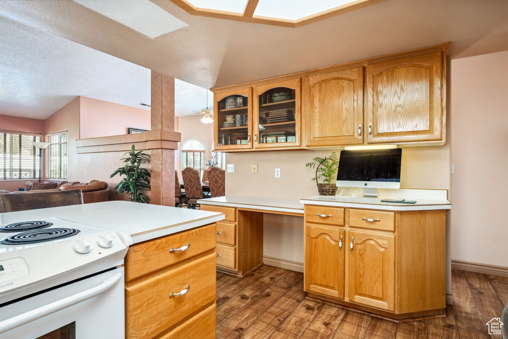 Kitchen with vaulted ceiling, white range with electric cooktop, wood finished floors, light countertops, and glass insert cabinets