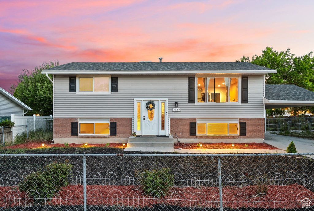 Raised ranch with a fenced front yard, brick siding, and an attached carport