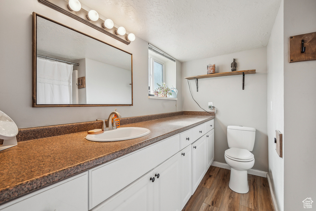 Bathroom featuring wood finished floors, vanity, toilet, a textured ceiling, and baseboards