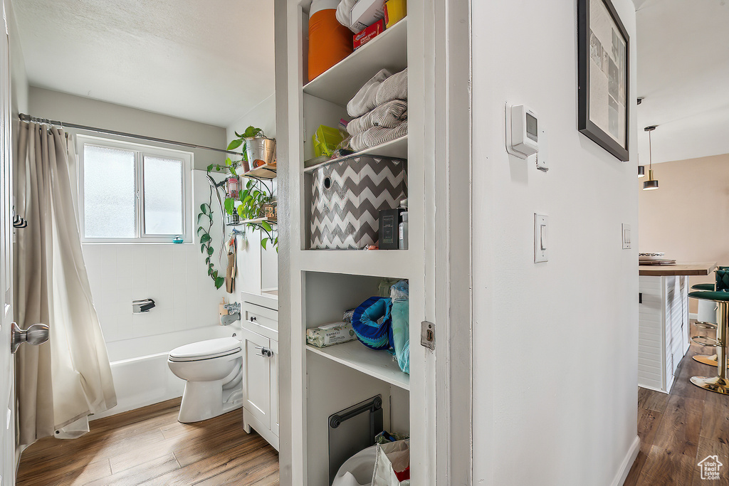 Full bath with wood finished floors, toilet, and shower / tub combo with curtain