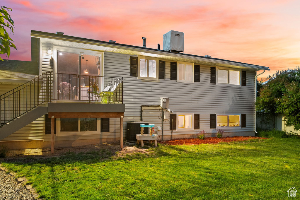 Back of property at dusk featuring cooling unit, a lawn, and stairs