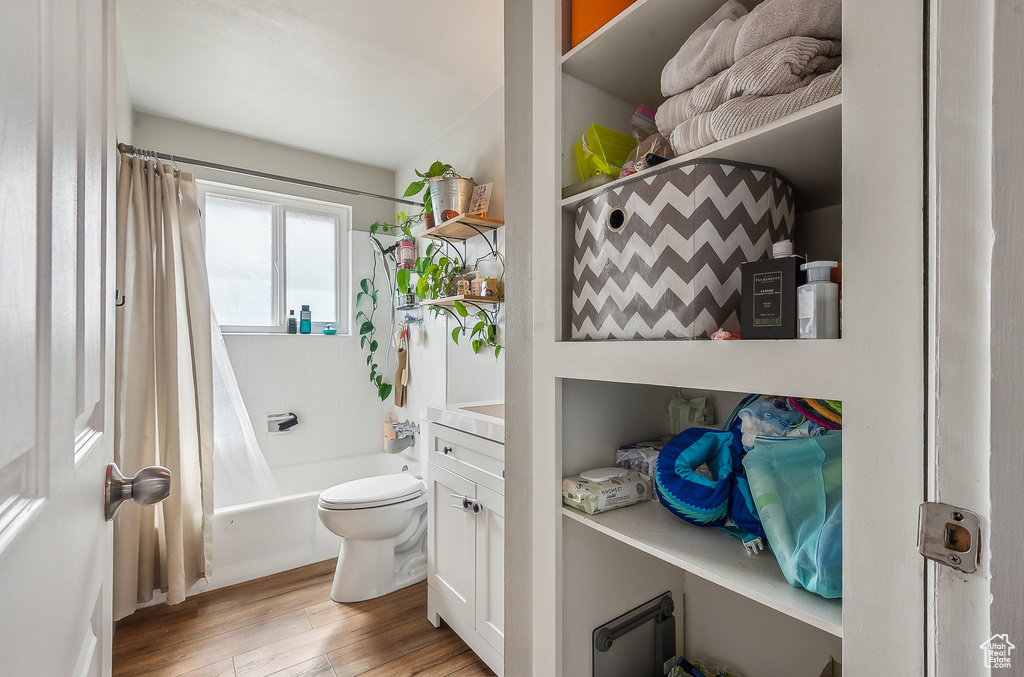Full bath featuring wood finished floors, shower / bath combination with curtain, and toilet