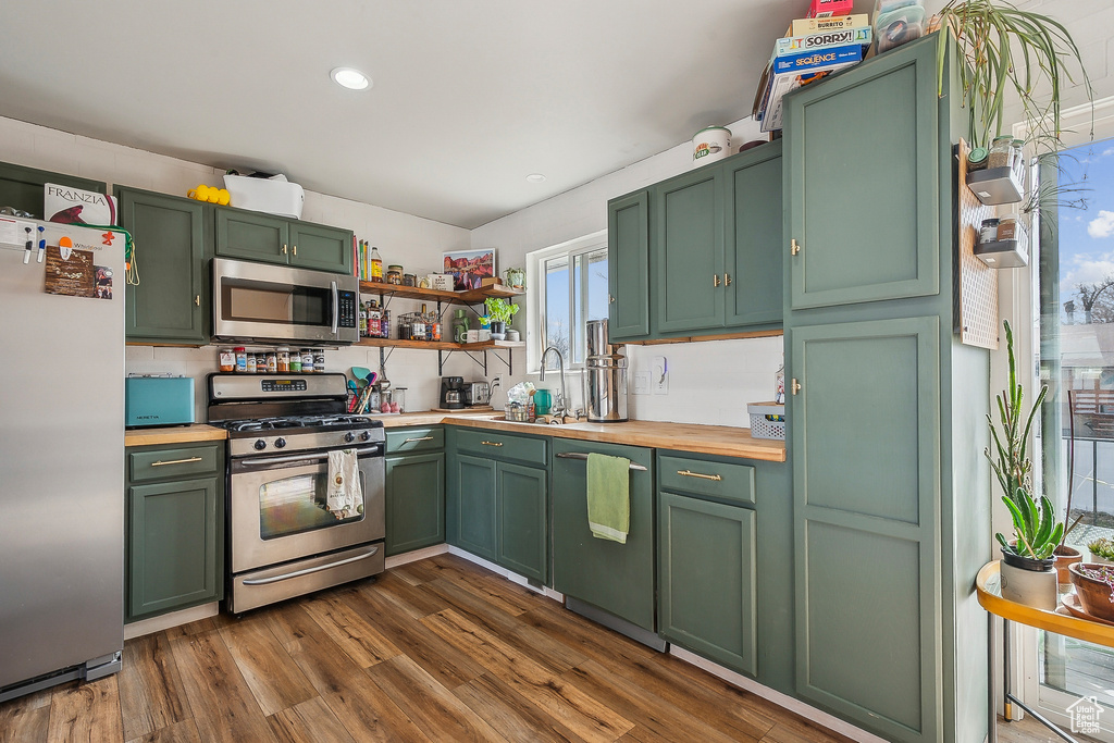 Kitchen with appliances with stainless steel finishes, green cabinets, a sink, dark wood-type flooring, and butcher block countertops