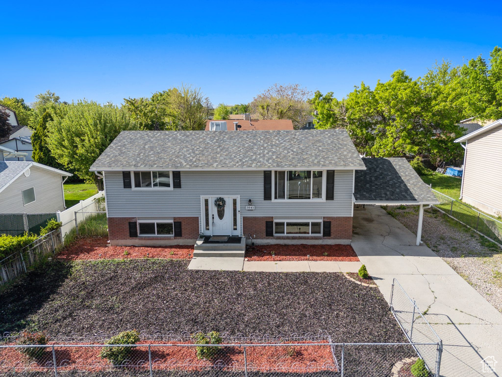 Split foyer home featuring brick siding, driveway, a carport, and a shingled roof