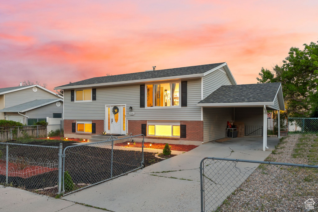 Bi-level home with concrete driveway, brick siding, a fenced front yard, an attached carport, and a gate