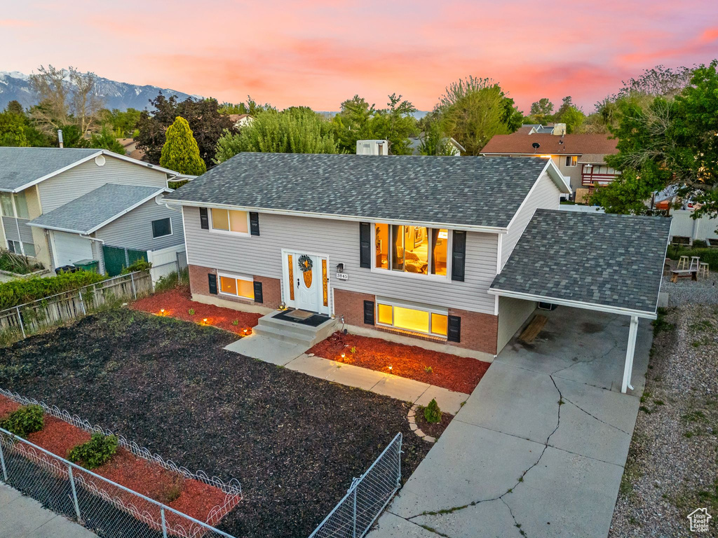 Bi-level home featuring driveway, roof with shingles, an attached carport, a mountain view, and brick siding