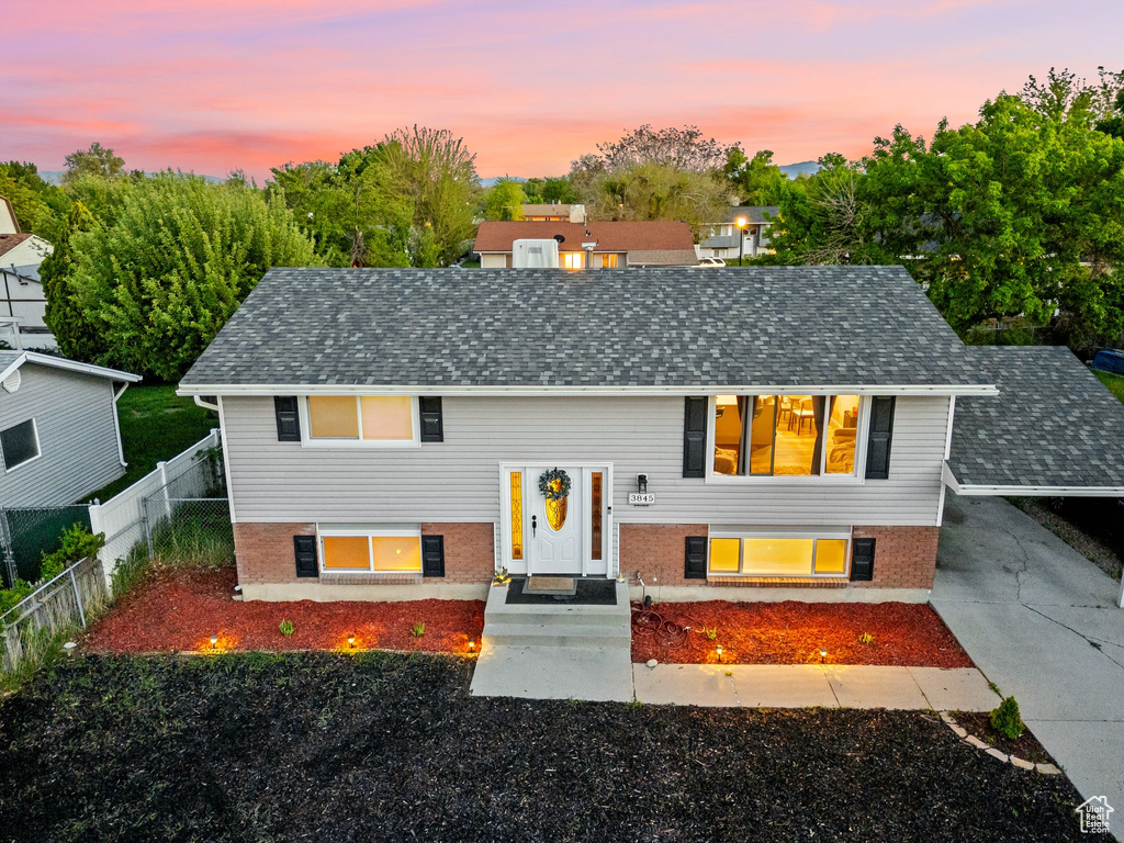 Raised ranch featuring roof with shingles, fence, and brick siding