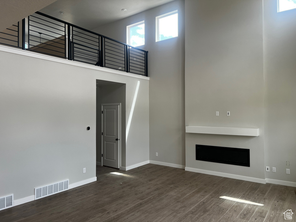 Unfurnished living room featuring wood finished floors, a high ceiling, baseboards, and a fireplace