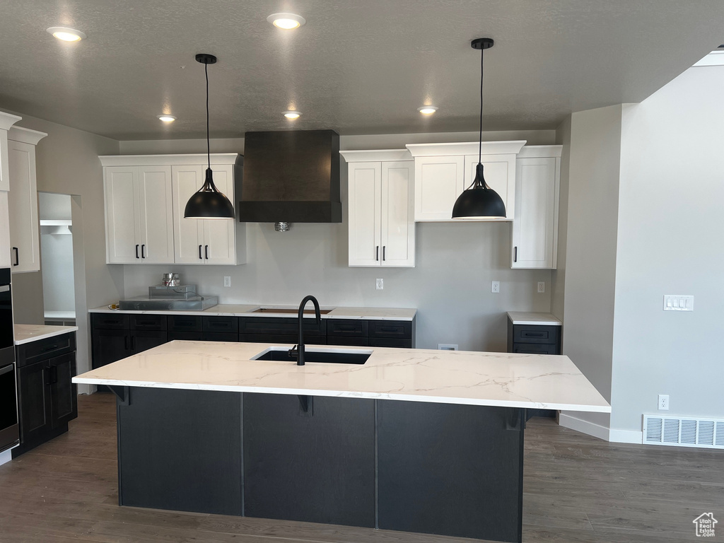 Kitchen with wall chimney exhaust hood, a sink, dark wood finished floors, a kitchen island with sink, and recessed lighting