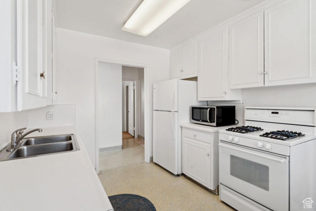 Kitchen with white appliances, a sink, white cabinetry, and light countertops